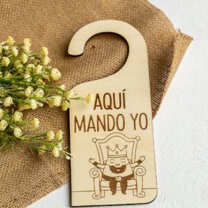 Colgador de puerta modelo Rey Aquí Mando Yo sobre fondo de tela de saco.