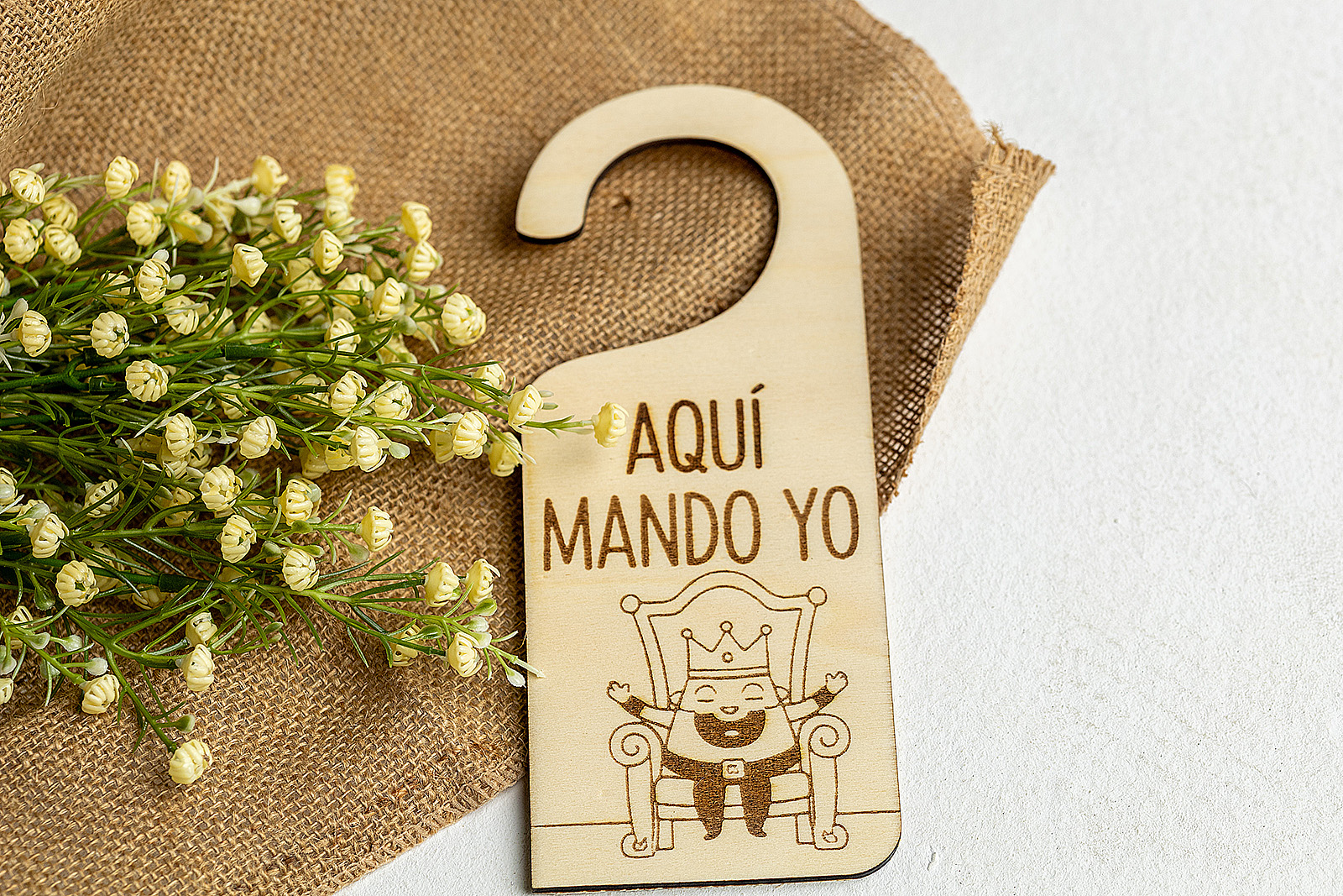 Colgador de puerta modelo Rey Aquí Mando Yo sobre fondo de tela de saco.