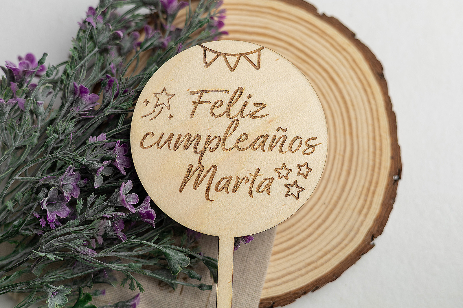 Topper de madera para tarta, personalizado con el grabado a láser "Feliz cumpleaños Marta", presentado junto a su bolsa de lino sobre una rodaja de madera.