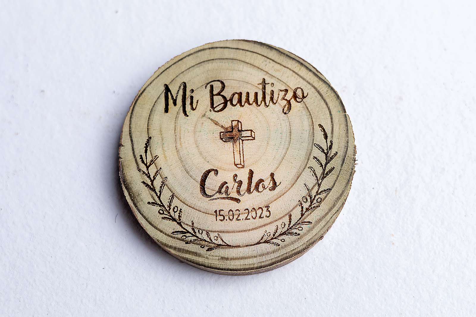 Imán rústico de madera para recuerdo de bautizo, con un grabado láser de una cruz dentro de una corona de laurel y personalizado con el nombre Carlos.