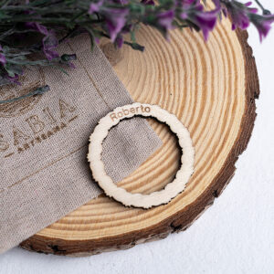 Presentación de marcasitios y servilletero de madera rústico personalizado, sobre rodaja de tronco con flores y bolsa de lino, ideal para decoración de mesas de boda.
