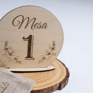 Número de mesa de madera redondo para boda, grabado con el número 1 y detalles florales, presentado con decoración natural.