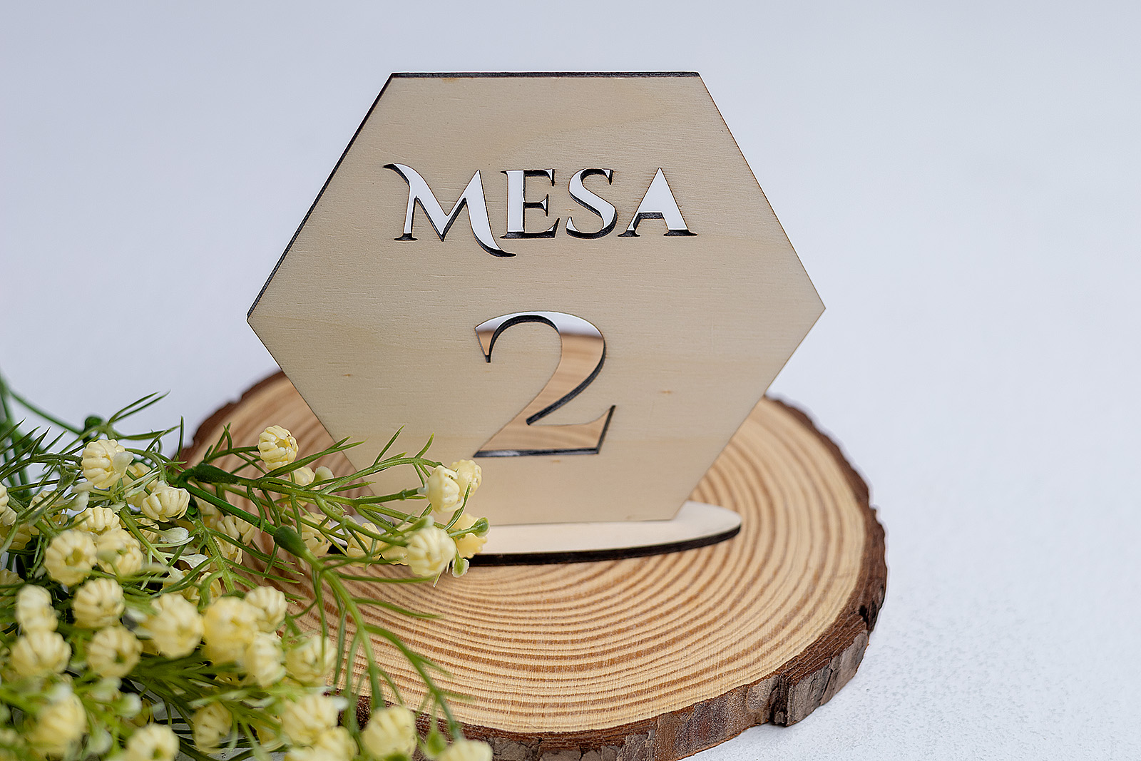 Número de mesa hexagonal de madera para boda, con diseño moderno calado del número 2 y decoración floral blanca y verde.