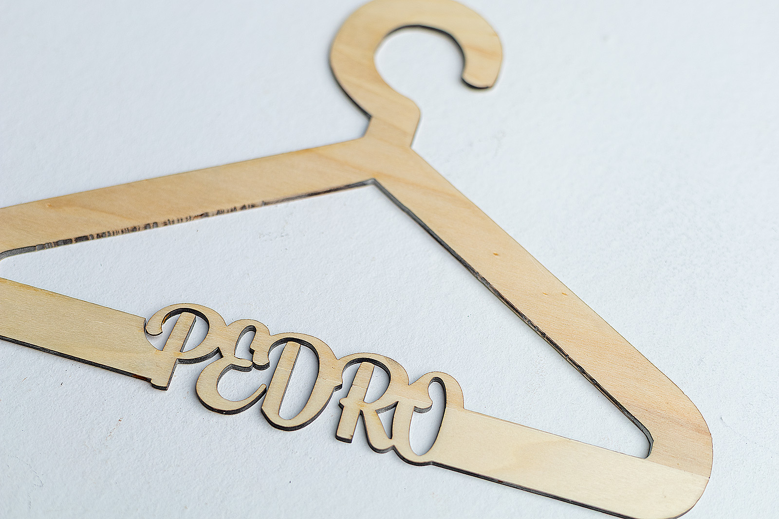 Primer plano del nombre Pedro cortado a láser en la barra inferior de una percha infantil de madera, mostrando la precisión del diseño.