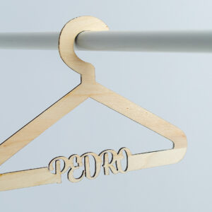 Percha infantil de madera colgada en una barra blanca, con el nombre Pedro calado en la estructura. Diseño original para regalo de nacimiento.