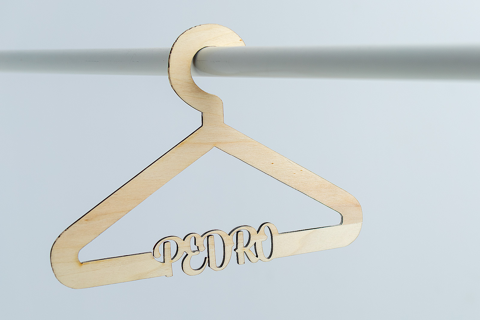 Percha infantil de madera colgada en una barra blanca, con el nombre Pedro calado en la estructura. Diseño original para regalo de nacimiento.