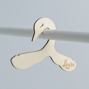 Percha infantil de madera con forma de cisne colgada en una barra blanca, personalizada con el nombre Laura. Diseño elegante para armario infantil.