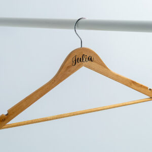 Percha de madera personalizada con nombre grabado a láser colgada en una barra blanca, ideal para las fotos del vestido de novia.