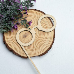 Gafas redondas de madera con varilla, estilo Harry Potter, presentadas sobre una rodaja de madera con flores, ideal para photocall de bodas.