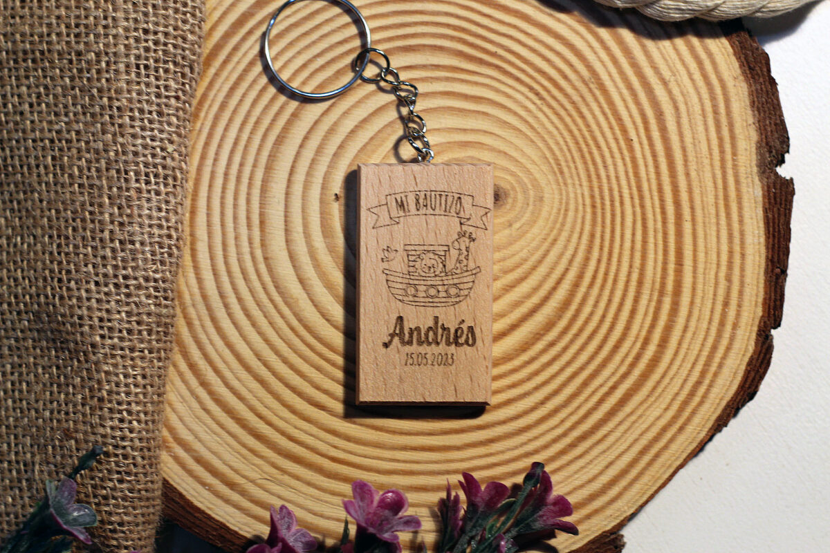 Llavero de madera para recuerdo de bautizo con diseño del Arca de Noé y nombre Andrés, presentado sobre una rodaja de tronco y tela de saco para un estilo rústico.