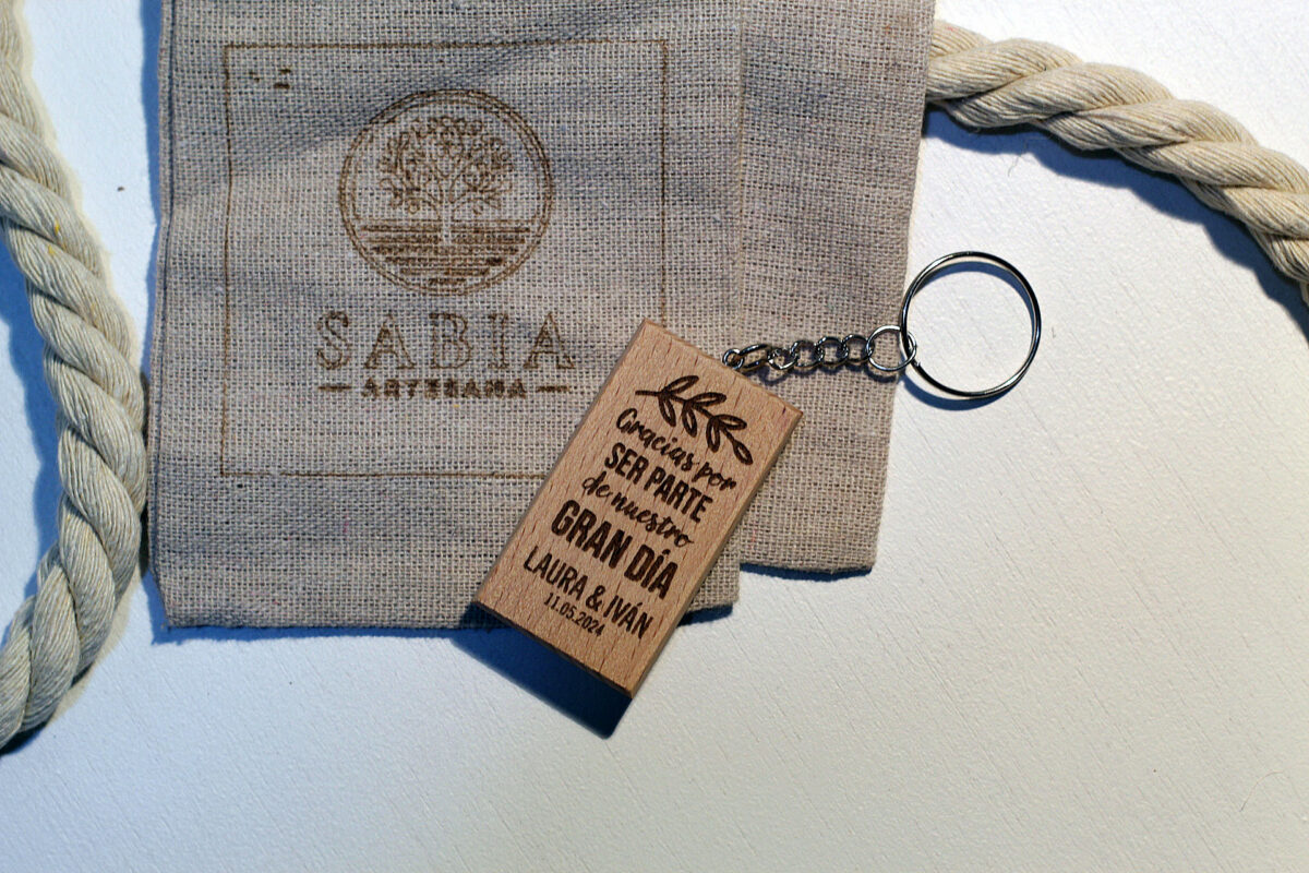 Detalle de boda de agradecimiento: llavero de madera grabado de Sabia Artesana junto a su bolsa de lino.