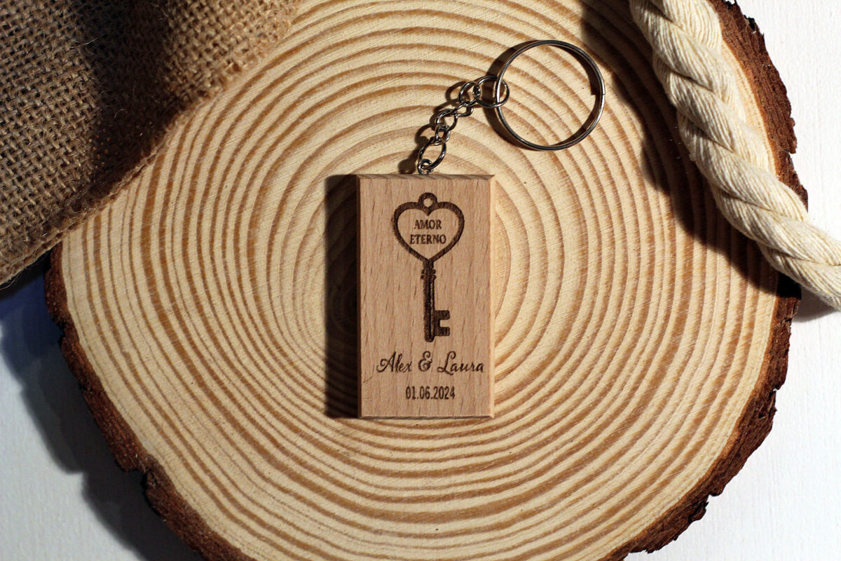 Llavero de madera para regalo de invitados de boda, con grabado láser de llave antigua y nombres de los novios, presentado sobre una base de madera rústica.