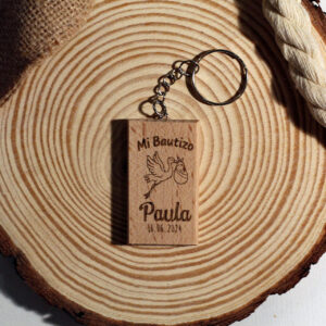 Recuerdo de bautizo original: Llavero de madera grabado con una cigüeña y el nombre del bebé, presentado sobre una base de madera rústica.