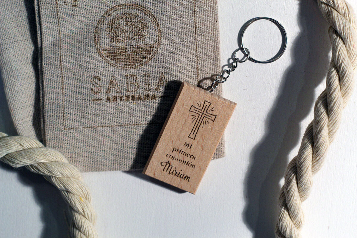 Recuerdo de comunión clásico con llavero de madera grabado, presentado junto a su bolsa de lino.