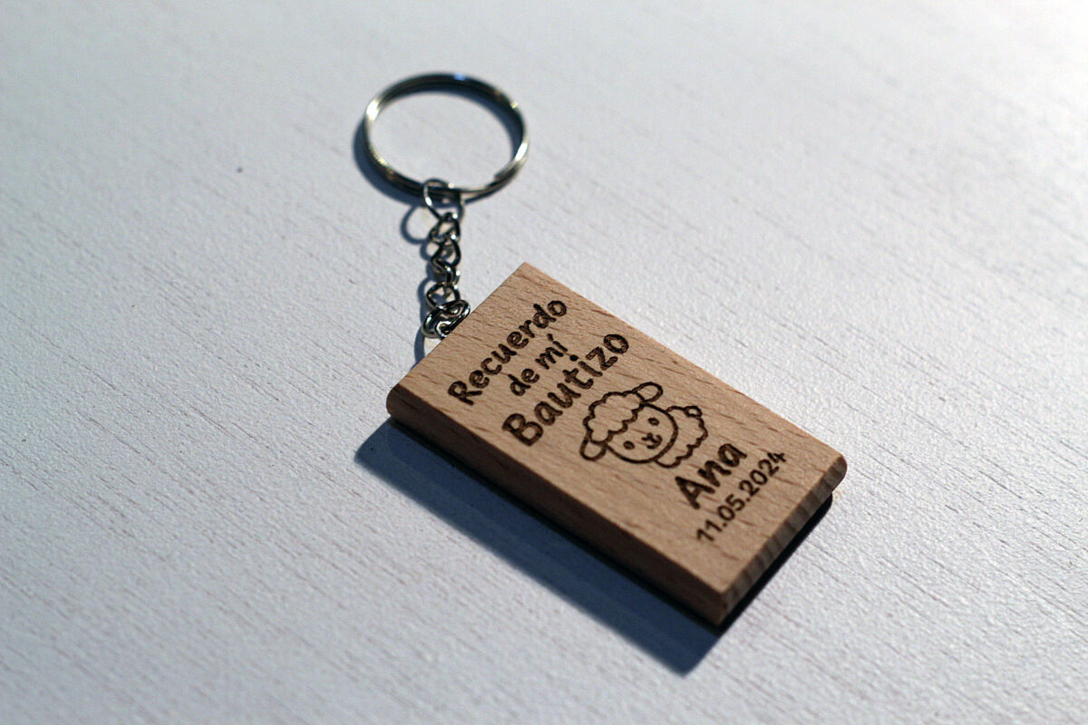 Vista en ángulo del llavero de bautizo de madera de haya mostrando su relieve y acabado.